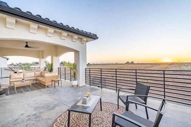 patio terrace at dusk with a balcony, ceiling fan, and an outdoor hangout area