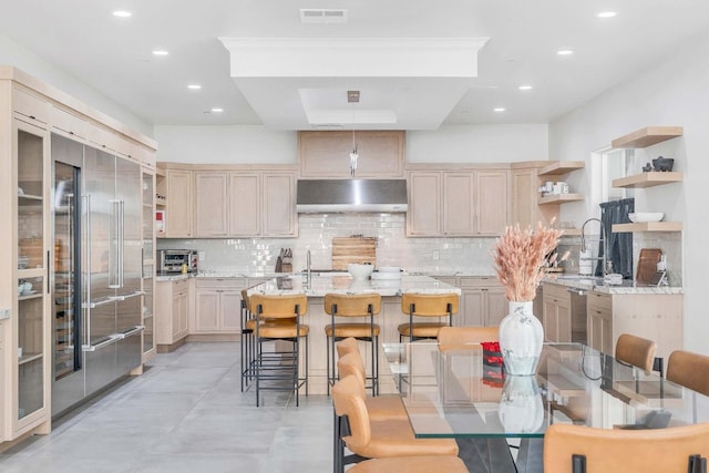 kitchen with a breakfast bar, light stone counters, light brown cabinets, and tasteful backsplash