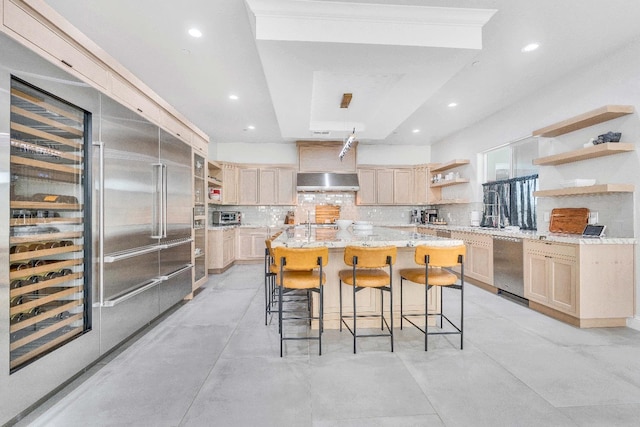 kitchen featuring a breakfast bar, decorative backsplash, appliances with stainless steel finishes, light brown cabinets, and extractor fan