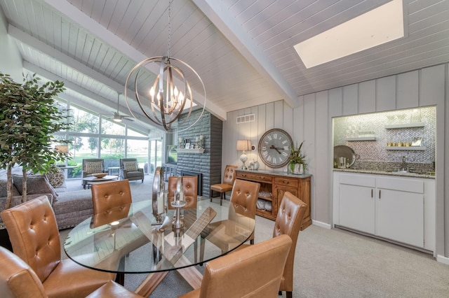 carpeted dining area with vaulted ceiling with beams, ceiling fan with notable chandelier, sink, and a brick fireplace