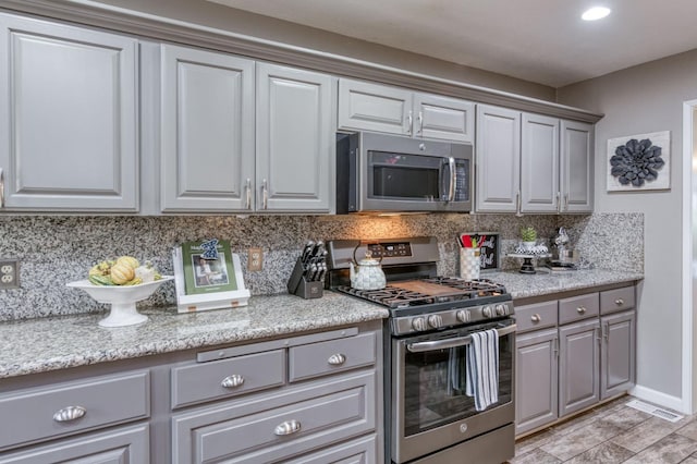 kitchen with light stone countertops, appliances with stainless steel finishes, gray cabinetry, and decorative backsplash