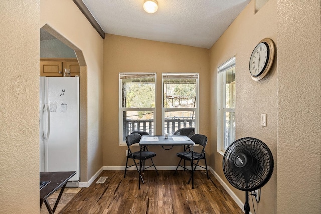 sitting room featuring dark wood-type flooring, a textured ceiling, baseboards, arched walkways, and a textured wall