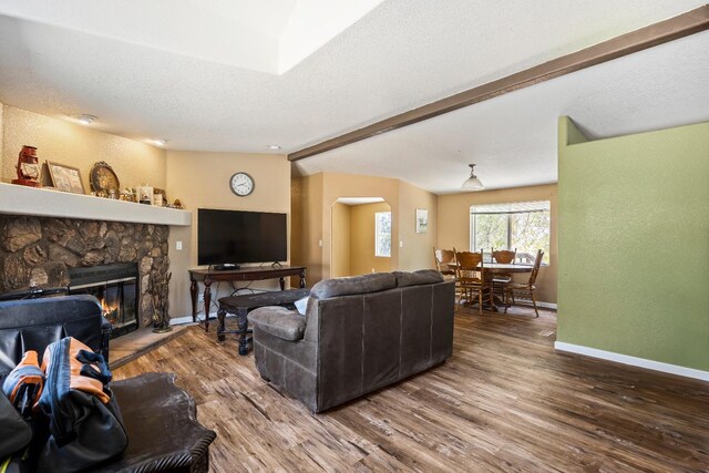 living room featuring a textured ceiling, a stone fireplace, and hardwood / wood-style flooring