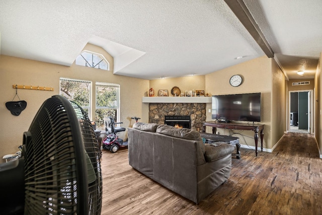 living room with vaulted ceiling with beams, wood-type flooring, a stone fireplace, and a textured ceiling