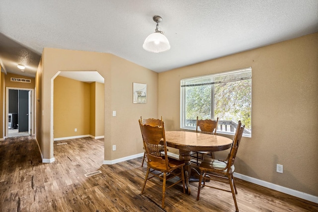 dining area with lofted ceiling, a textured ceiling, and hardwood / wood-style flooring