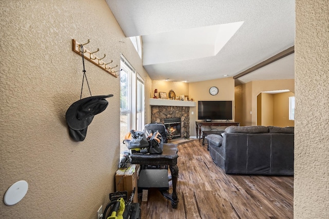 living room with a textured ceiling, hardwood / wood-style floors, and a stone fireplace