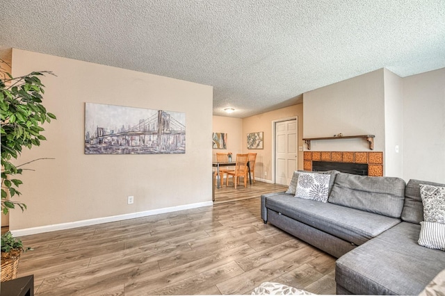 living area with a tiled fireplace, a textured ceiling, baseboards, and wood finished floors