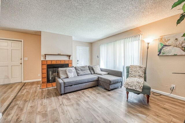 living area featuring a textured ceiling, a tile fireplace, light wood-style flooring, and baseboards