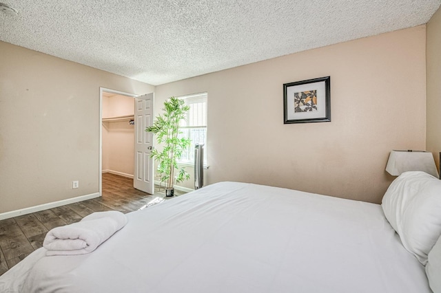 bedroom featuring a textured ceiling, wood finished floors, baseboards, a closet, and a walk in closet