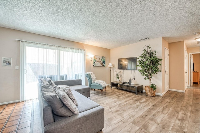 living room with light wood-type flooring, baseboards, visible vents, and a textured ceiling