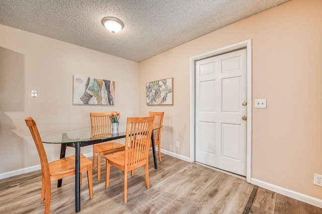 dining room with light wood-style floors, baseboards, and a textured ceiling