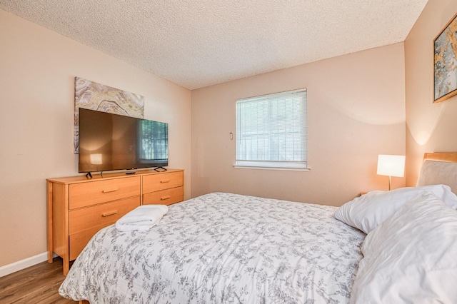 bedroom with a textured ceiling, baseboards, and wood finished floors