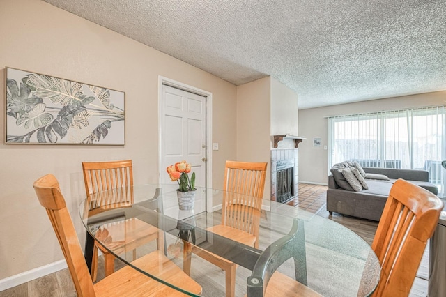 dining area featuring a textured ceiling, a fireplace, wood finished floors, and baseboards