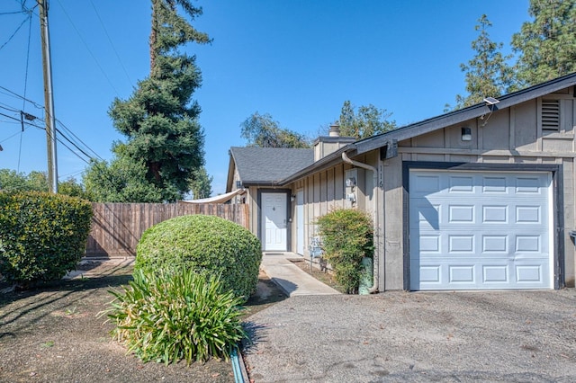 view of front of home featuring a garage, fence, driveway, board and batten siding, and a chimney