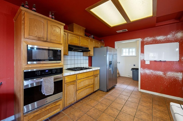 kitchen featuring decorative backsplash, appliances with stainless steel finishes, tile counters, and light tile patterned floors