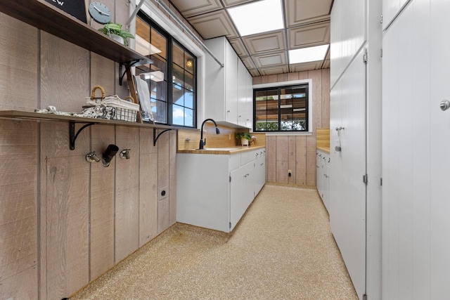 kitchen with sink, white cabinets, and wood walls