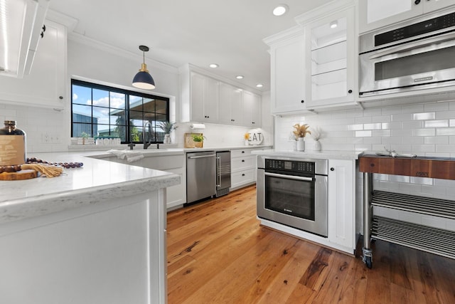 kitchen featuring pendant lighting, tasteful backsplash, white cabinetry, ornamental molding, and stainless steel oven