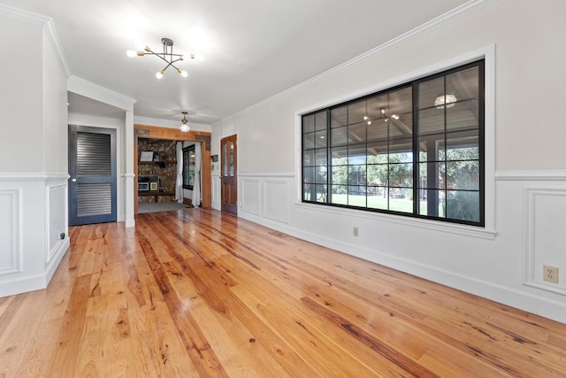 unfurnished living room featuring crown molding, a fireplace, a chandelier, and light wood-type flooring