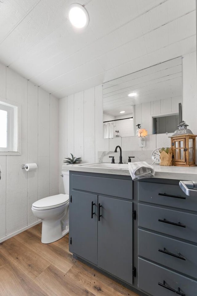 bathroom featuring hardwood / wood-style flooring, vanity, wooden walls, and toilet