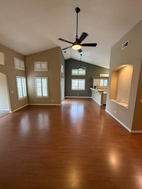 unfurnished living room featuring dark hardwood / wood-style floors, ceiling fan, a wealth of natural light, and vaulted ceiling