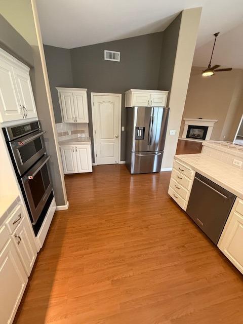 kitchen featuring light wood-type flooring, stainless steel appliances, ceiling fan, high vaulted ceiling, and white cabinets