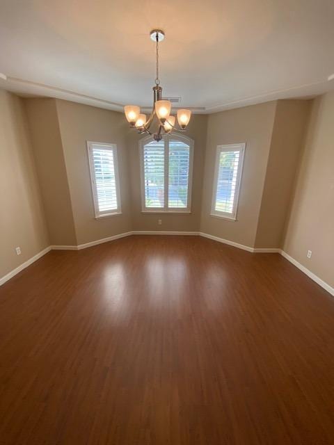 empty room with dark hardwood / wood-style floors and a notable chandelier