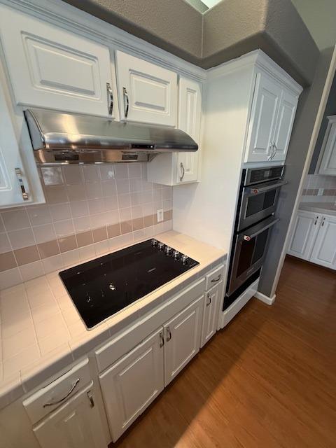 kitchen featuring backsplash, black electric cooktop, wood-type flooring, tile countertops, and white cabinets