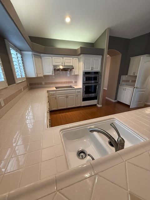 kitchen featuring black electric stovetop, tile countertops, white cabinetry, and tasteful backsplash