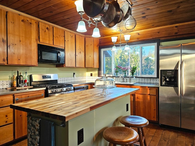 kitchen featuring hanging light fixtures, appliances with stainless steel finishes, wooden counters, and a kitchen island