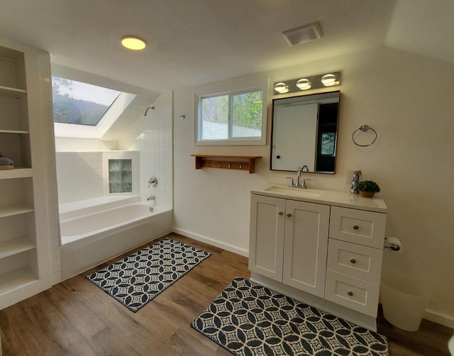 bathroom featuring hardwood / wood-style flooring, lofted ceiling with skylight, vanity, and bathing tub / shower combination