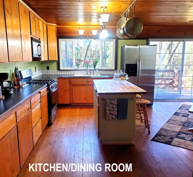 kitchen with light hardwood / wood-style floors, wooden ceiling, appliances with stainless steel finishes, decorative light fixtures, and sink