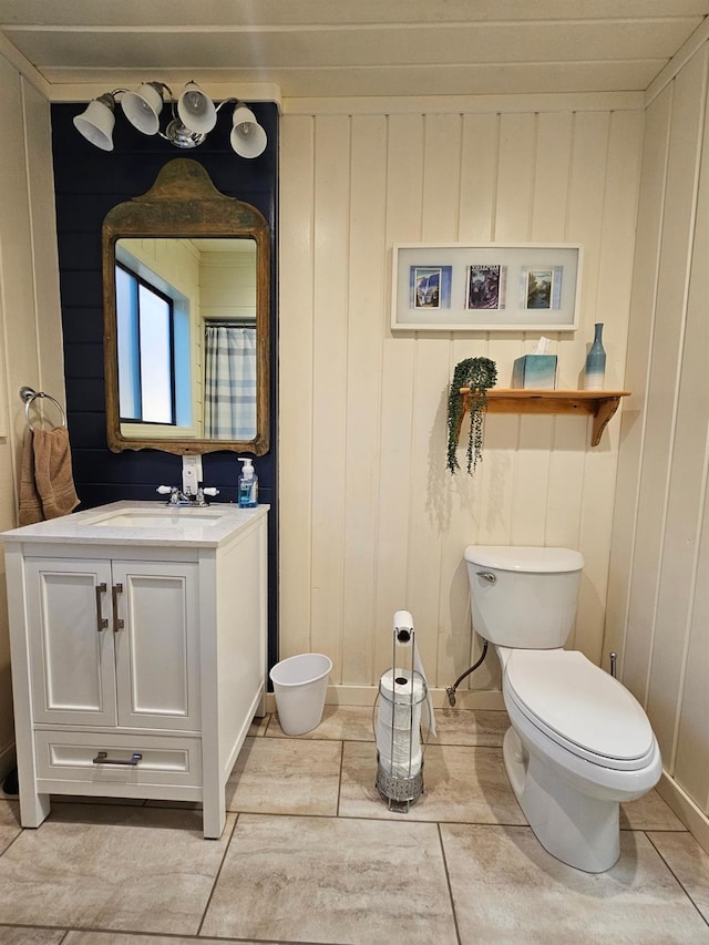 bathroom with toilet, wood walls, and vanity