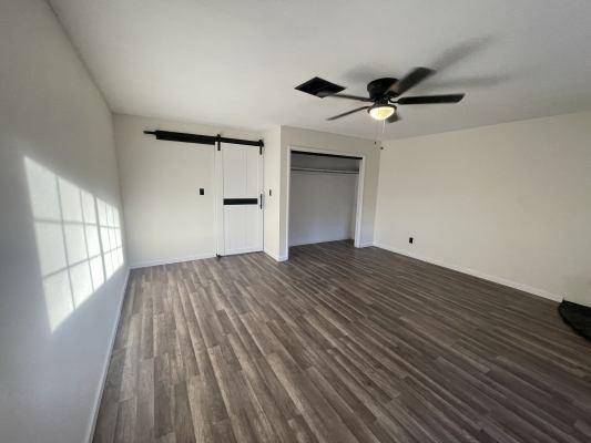 unfurnished bedroom featuring ceiling fan, a closet, dark hardwood / wood-style floors, and a barn door