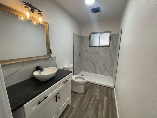 bathroom with a tile shower, vanity, toilet, and hardwood / wood-style flooring