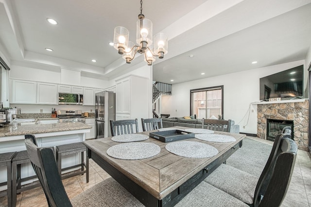 tiled dining room featuring a notable chandelier, a raised ceiling, and a fireplace