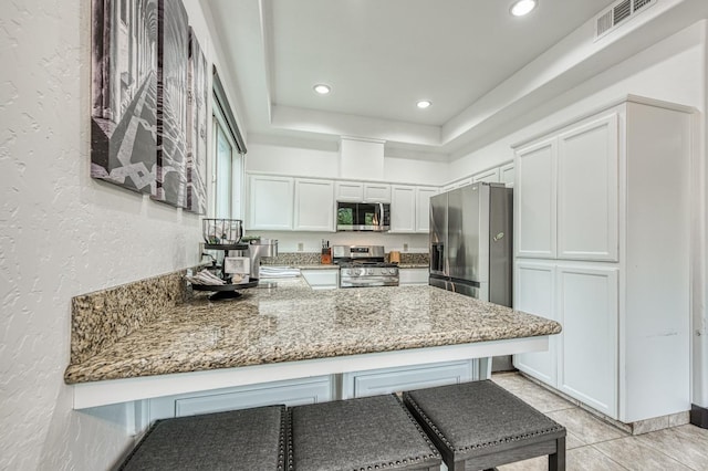 kitchen with light stone countertops, appliances with stainless steel finishes, kitchen peninsula, and white cabinetry