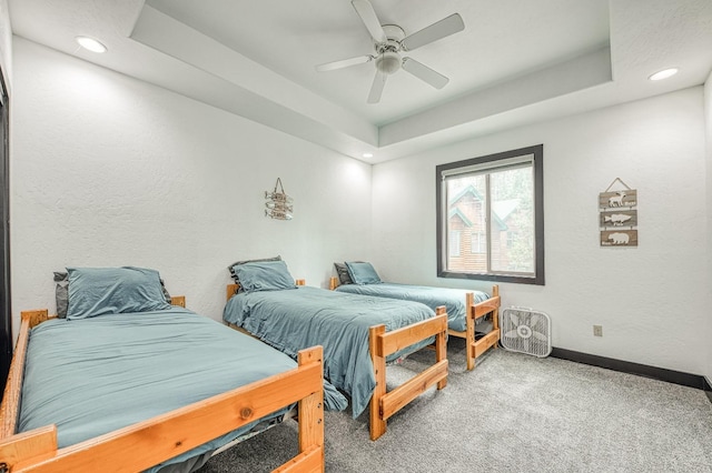 carpeted bedroom featuring ceiling fan and a raised ceiling