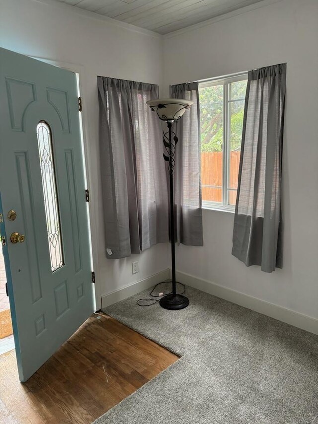 foyer with wood ceiling, crown molding, and carpet