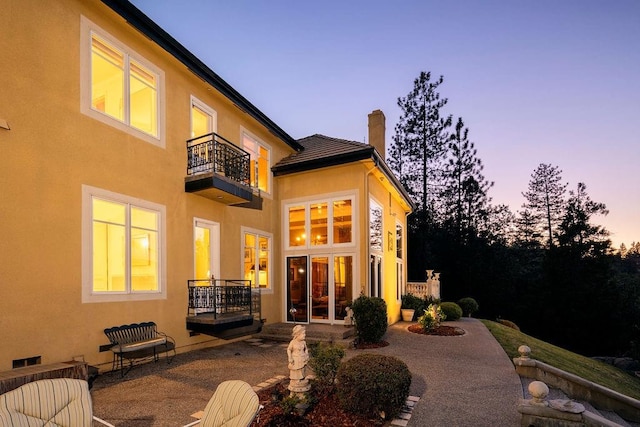 back house at dusk with a balcony and a patio area