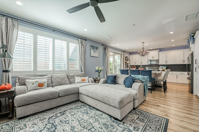 living room with plenty of natural light, ceiling fan with notable chandelier, and light wood-type flooring