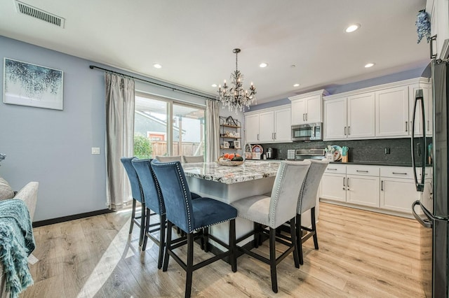 kitchen featuring stainless steel appliances, hanging light fixtures, backsplash, and light wood-type flooring