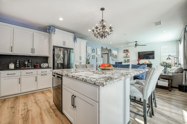 kitchen featuring an island with sink, light stone counters, stainless steel fridge, sink, and decorative light fixtures