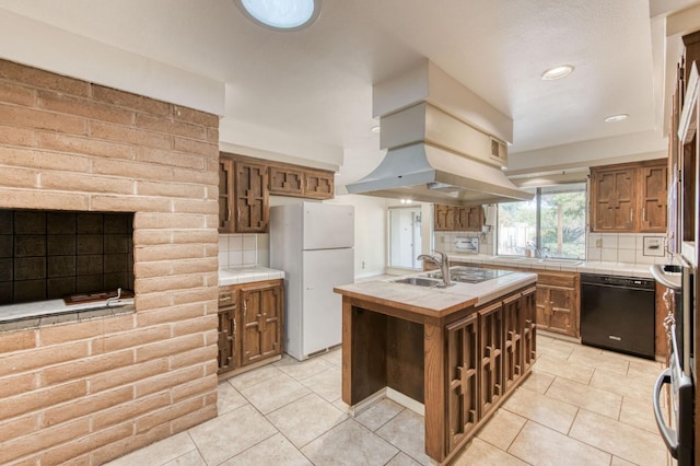 kitchen with tasteful backsplash, white refrigerator, black dishwasher, a center island with sink, and tile countertops