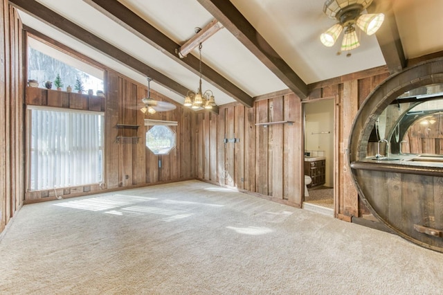 carpeted empty room featuring ceiling fan with notable chandelier, lofted ceiling with beams, and wooden walls