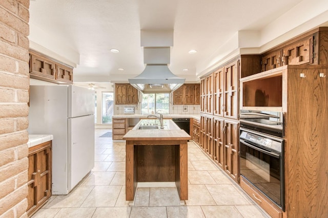 kitchen with light tile patterned floors, sink, a kitchen island with sink, backsplash, and black appliances