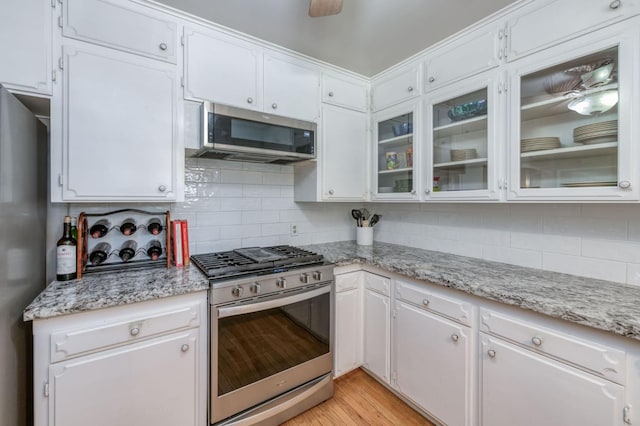 kitchen with decorative backsplash, appliances with stainless steel finishes, light wood-type flooring, light stone countertops, and white cabinetry