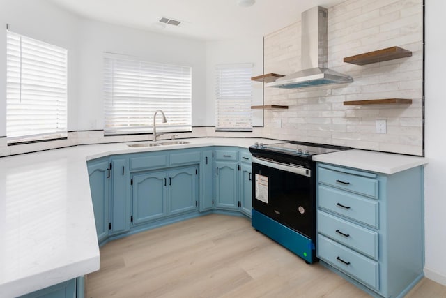 kitchen featuring black range with electric cooktop, wall chimney range hood, sink, light hardwood / wood-style floors, and blue cabinetry