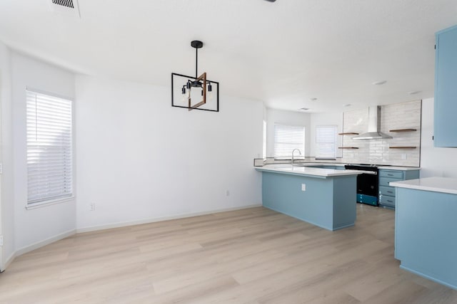 kitchen featuring kitchen peninsula, light hardwood / wood-style flooring, range, pendant lighting, and wall chimney exhaust hood