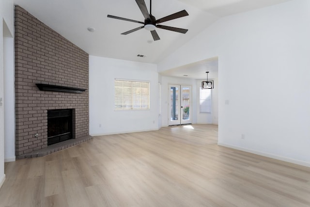 unfurnished living room featuring french doors, vaulted ceiling, a brick fireplace, light hardwood / wood-style floors, and ceiling fan