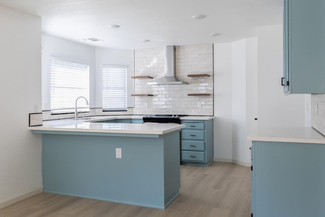 kitchen with wall chimney range hood, tasteful backsplash, light hardwood / wood-style floors, and kitchen peninsula